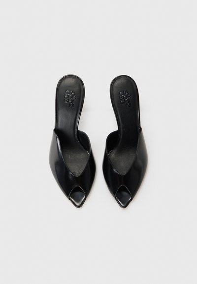Mules ouverts en cuir noir avec un bout pointu et un design de vamp découpé. Texture lisse et style minimaliste. Conception à enfiler sans embellissements.