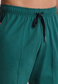 Groene joggingsbroek van zacht materiaal met een elastische tailleband, trekkoord en zijzakken. Heeft een gladde textuur en een relaxte pasvorm.
