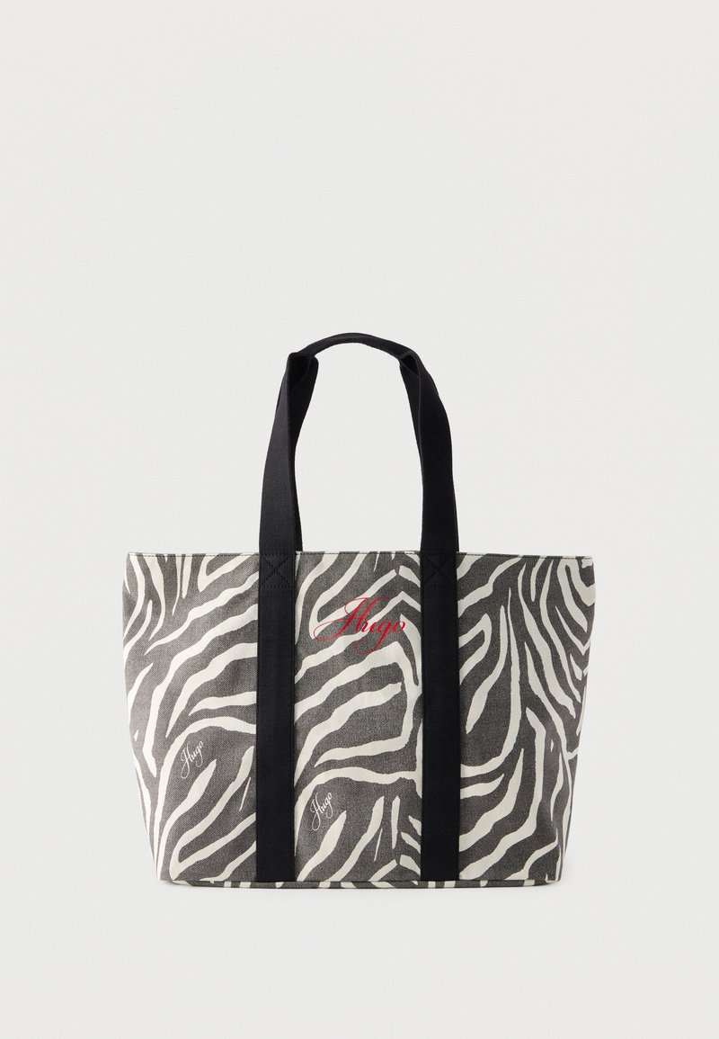 Υφασμάτινη τσάντα tote με ασπρόμαυρες ρίγες ζέβρας, μαύρες λαβές και κόκκινη κεντημένη επιγραφή "Hugo" στο μπροστινό μέρος.