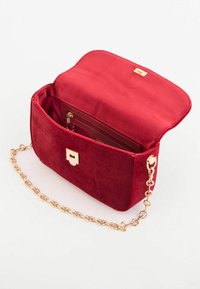 Czerwona zamszowa torebka na ramię z klapką, złotymi elementami i łańcuszkowym paskiem. Wnętrze zawiera kieszeń na zamek i miejsce na karty.