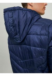 Námořnická pufovaná bunda s kapucí, která se pyšní prošívaným designem a lesklou tkaninou. Výrazné diagonální švy a elastické detaily na okrajích.