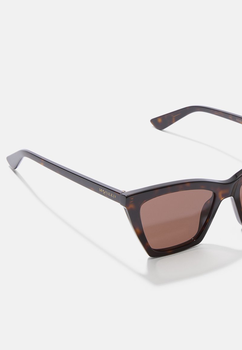 Occhiali da sole quadrati in tartaruga con lenti marroni e aste sottili, vista angolata su sfondo bianco.