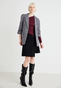 Sivi karirani sako, bordo majica, crna plisirana suknja i crne čizme do koljena s potpeticama. Glatki materijal s strukturiranim dizajnerskim elementima.