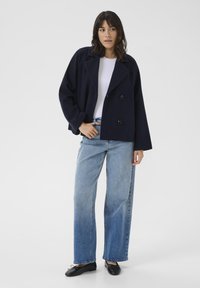 Jūrinė dublio užsegama striukė su plačiais atlapais, derinama su šviesiai mėlynais plačiais džinsais ir juodais butais. Lygus audinys su minimaliais dekorais.