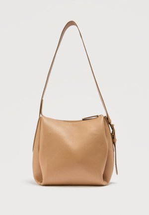 Δερμάτινη τσάντα ώμου σε καφέ χρώμα με ρυθμιζόμενο ιμάντα και κλείσιμο με φερμουάρ, σε όρθια θέση πάνω σε απλό φωτεινό φόντο.