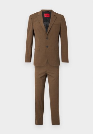 Ensemble marron comprenant un blazer à deux boutons et un pantalon assorti. Présente un tissu texturé, des revers en pointe et des poches plaquées. Étiquette de marque rouge visible.