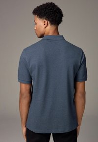 Polo oscuro de color azul, hecho de tela texturizada, con cuello y mangas cortas, visto desde la parte posterior, con un dobladillo recto.