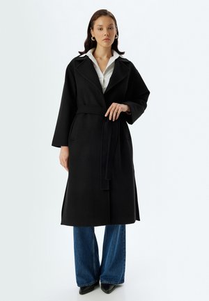 Cappotto lungo nero con design avvolgente, ampi revers e cintura da annodare. Presenta maniche dritte e due tasche laterali. Texture liscia.