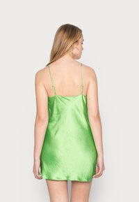 Vestido mini de cetim verde com alças finas ajustáveis, textura suave e um leve brilho, criando uma silhueta ajustada até a metade da coxa.