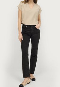 Beige v-neck top with short sleeves, black straight-leg jeans, and beige flats with black toe caps. Smooth texture and fitted silhouette.