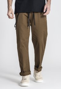Lichtbruine, ruime broek met een elastische tailleband, zwarte trekkoorden en opgerolde boorden, gecombineerd met lichtgekleurde sneakers.