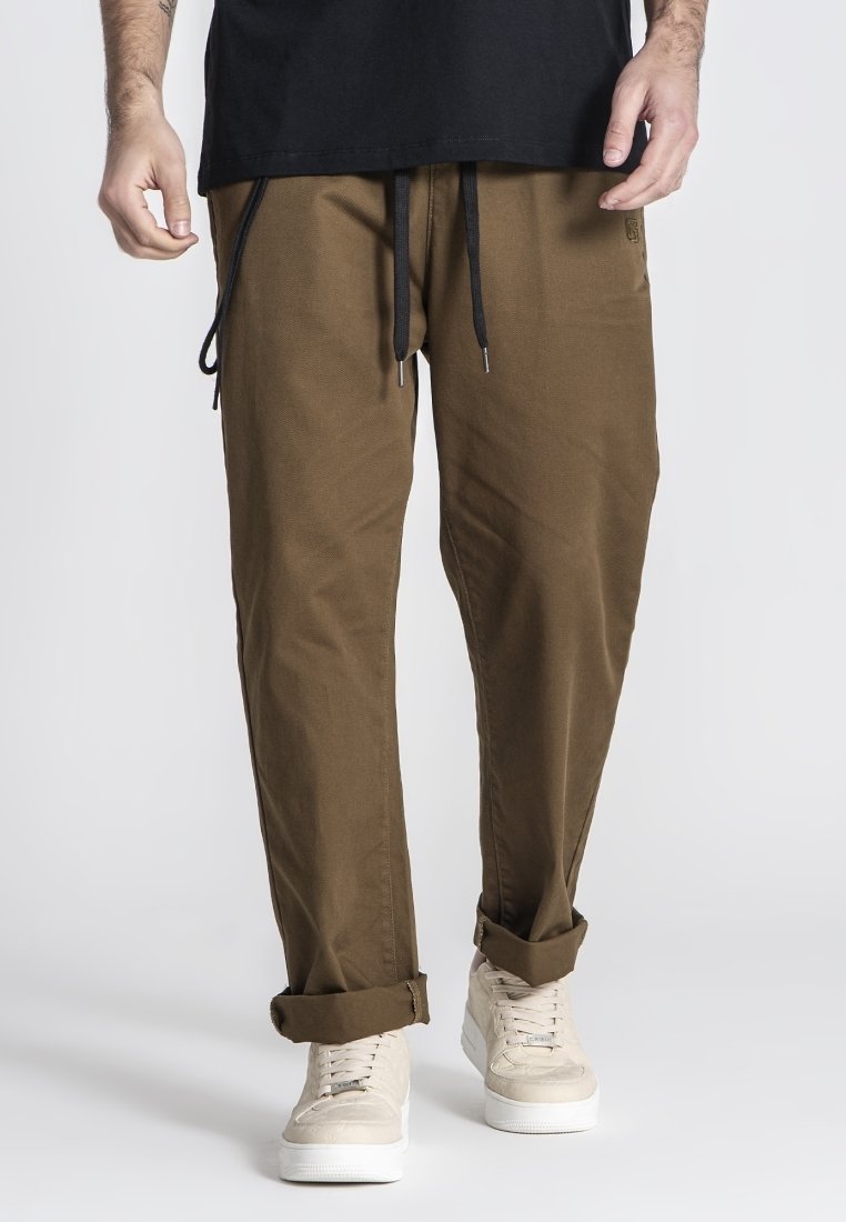Lichtbruine, ruime broek met een elastische tailleband, zwarte trekkoorden en opgerolde boorden, gecombineerd met lichtgekleurde sneakers.
