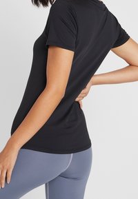 Svart tajt träningsskjorta med korta ärmar, slät textur och rundad halsringning, i kombination med ljusgrå leggings med rosa sömmar.