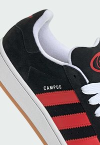 Sneaker in suede nero con strisce rosse, lacci bianchi e suola in gomma bianca. Logo "CAMPUS" stampato in bianco sul lato. Materiali lavorati.