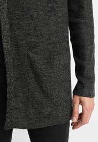 Mörkgrå stickad cardigan med en texturerad yta, med en framficka och ribbade ärmslut, öppen design framtill.
