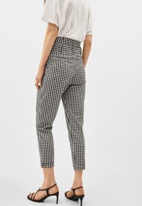 Hochgeschnittene, schwarz-weiße Gingham-Karottenhosen mit schmaler Passform und verkürzter Länge, kombiniert mit schwarzen, schmalen, hohen Sandalen.