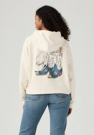 Felpa crema con grafica di stivali da cowboy e un cappello sul retro. Il tessuto è morbido con una vestibilità comoda e una tasca a marsupio.
