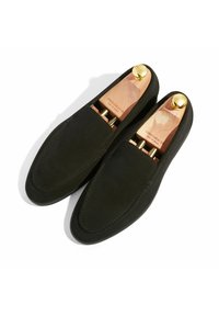 Zwarte suède loafers met een gladde afwerking, voorzien van een ronde neus en houten schoenleestrammen met messing knoppen aan de binnenkant. Minimalistische stikdetails.