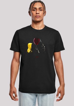 Black cotton t-shirt featuring a graphic design with a yellow hooded figure and a red balloon, styled with a horror theme and bold colors.
