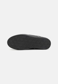 Black sneaker sole with a textured rubber surface featuring a grid pattern and embossed logo details, providing grip and durability.