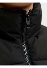 Chaqueta de plumas negra con cuello alto, textura suave y cremallera central con tira de agarre mate y costuras en contraste.