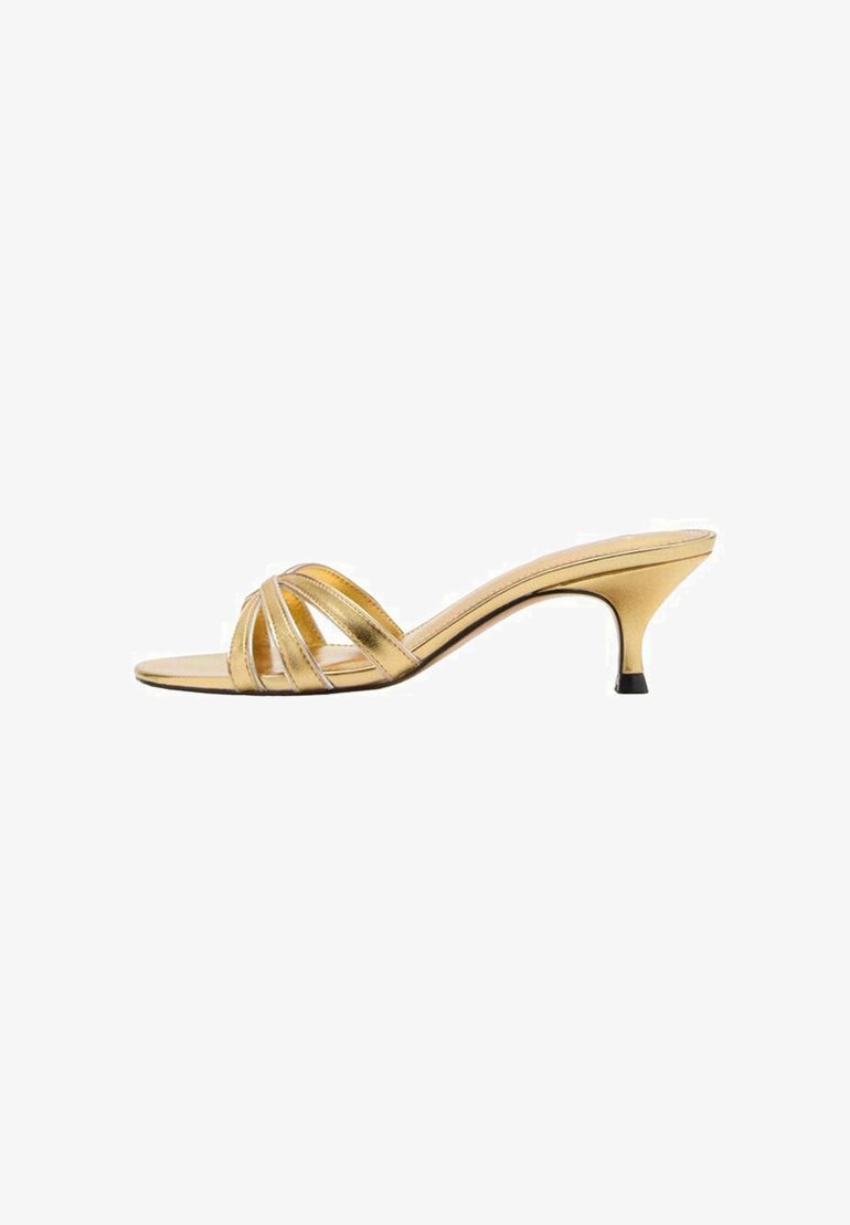 Mules à talons hauts métalliques dorés avec trois brides croisées, une pointe effilée et un accent noir sur le talon mince. Fini lustre.