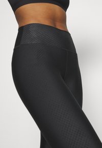 Black high-waisted leggings with a textured pattern, featuring a smooth waistband and snug fit. Made from stretchy, opaque material.
