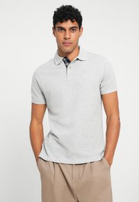 Πόλο μπλούζα κοντομάνικη, γκρι, φτιαγμένη από βαμβάκι, με γιακά και καρό σχέδιο κάτω από τον γιακά.