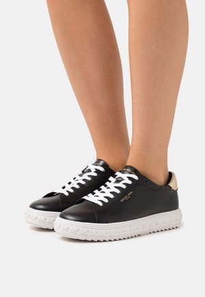 Schwarze Ledersneaker mit weißen Schnürsenkeln, einem goldfarbenen Detail an der Ferse und einer strukturierten weißen Sohle mit Logomuster.