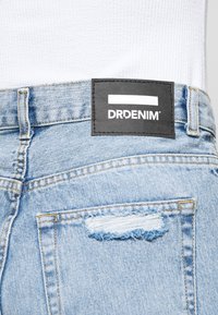 Jasnoniebieskie dżinsy z drobnym przetarciem na tylnej kieszeni oraz czarną naszywką marki DRDENIM na pasku.