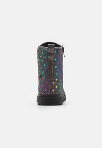 Botín negro hasta el tobillo con una superficie texturizada y brillante, que presenta patrones de corazones multicolores, cremallera trasera y una suela de goma negra en contraste.