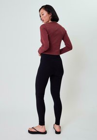 Pikad varrukad, burgundia tooniga topp, mis on koos mustade, kõrgelt taljes retuusidega. Sobivus on keha lähedane, sile tekstuur ja minimaalne disain.