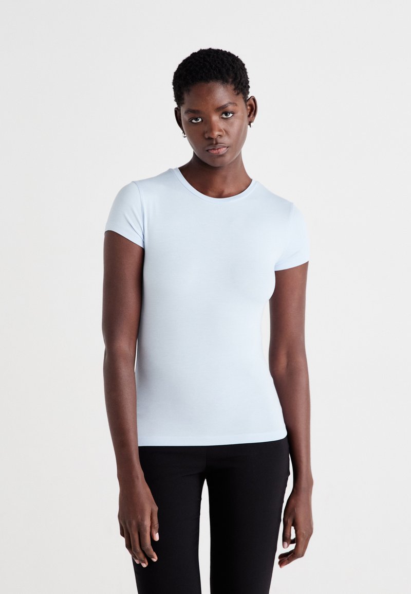 T-shirt azzurro chiaro a maniche corte con scollo rotondo, design aderente e texture liscia. Indossato con pantaloni neri. Stile semplice e classico.