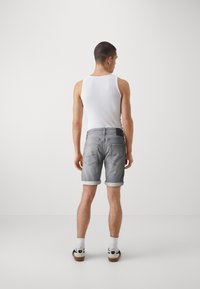 Chancletas de denim gris con puños enrollados, bolsillos traseros con detalles de costura, combinadas con una camiseta sin mangas blanca y calcetines deportivos.