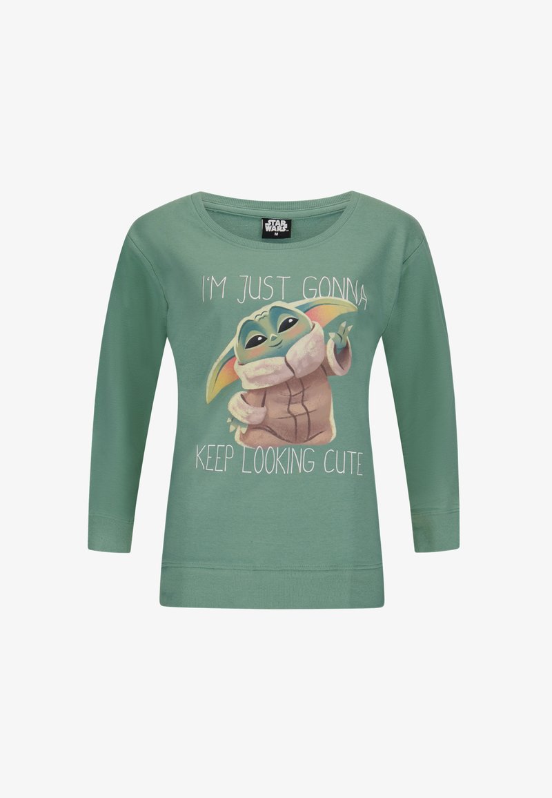 Chemise verte à manches longues avec un personnage de dessin animé aux grandes oreilles et le texte : « JE VAIS JUSTE CONTINUER À ÊTRE MIGNON. » Tissu doux, design décontracté.