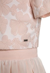 Różowa sukienka w odcieniu blush z haftowanymi kwiatowymi wzorami, teksturowanym gorsetem, gładkim paskiem w talii oraz warstwową spódnicą z tiulu z falbanką na krawędzi.