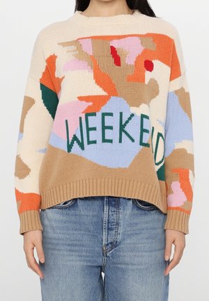 Sweter z abstrakcyjnym wielokolorowym wzorem i zielonym napisem „WEEKEND”, noszony z jasnoniebieskimi jeansami, pokazany od szyi do bioder.