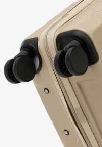 Valigia rigida beige con doppie ruote nere, superficie texturizzata e chiusura a zip. Accentuata da dettagli hardware neri.