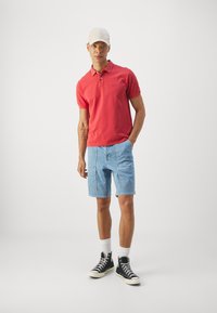 Rdeča kratka polo majica, svetlo modri denim kratki hlače, črne visoke superge, bele nogavice in bež kapa. Preprost dizajn in sproščen kroj.