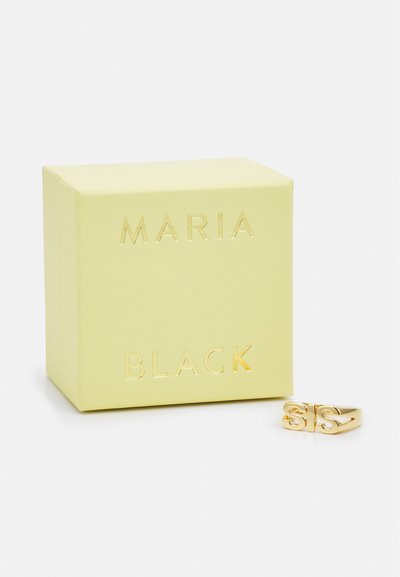 Zlatni prsten s dizajnom "SIS", odložen pored svijetlo žute četvrtaste kutije s utisnutim slovima "MARIA BLACK" u zlatnoj boji.