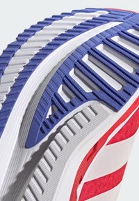 Rote und weiße Sportschuhsohle mit einer strukturierten blauen Gummigriff, geschichtetem weißen Zwischensohl und sichtbarem Profil für Traktion.