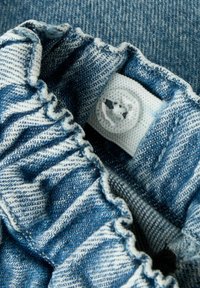 Kadriranje plavobijelih prugastih elastičnih denimski pojas sa prozirnim gumbom sašivenim na tkani oznaku.