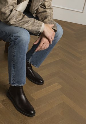 Bruine leren chelsea boots met een gladde afwerking, voorzien van een ronde neus en een dikke, platte zool, gecombineerd met lichtblauwe spijkerbroek.