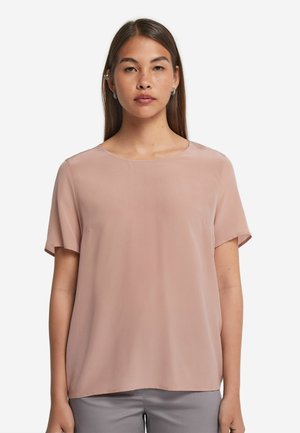 Ljus rosa kortärmad blus med rund halsringning, lätt tyg och lös passform, visad på en modell mot en vit bakgrund.