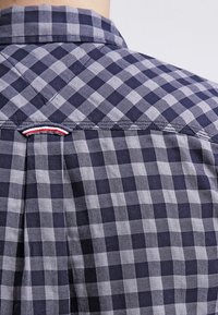 Marineblauw en grijs geruite shirt met een button-down kraag, een omgekeerde plooi aan de achterkant en een klein rood, wit en blauw labeldetail.