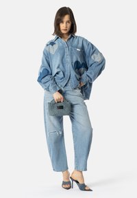 Denimskjorte med hjerteapplikasjoner, lys blå jeans med slitasje, vevd clutch-veske i teal, og åpne tå hæler i matchende nyanse.