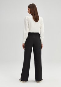 White long-sleeve blouse with buttoned cuffs paired with black wide-leg trousers featuring an elastic waistband. Textured fabric and straight fit.
