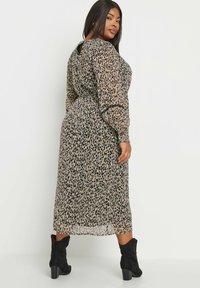 Pitkähihaista maxi-mekkoa, jossa on läpinäkyvä beige leopardikuvio, mustia yksityiskohtia, takana avainaukko ja joka on yhdistetty mustiin nilkkureihin.