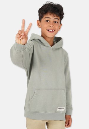 Vihreä huppari, joka on valmistettu pehmeästä kankaasta, sisältää etutaskun, resorikankaiset hihansuut ja tarran helmassa. Lapsi tekee rauhanmerkkiä.