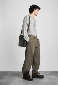 Light gray plaid shirt with a button-up design, paired with loose olive green trousers and brown lace-up boots. Black leather shoulder bag.